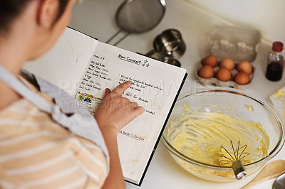 Buy stock photo Cropped shot of an unrecognizable woman using a family recipe while baking