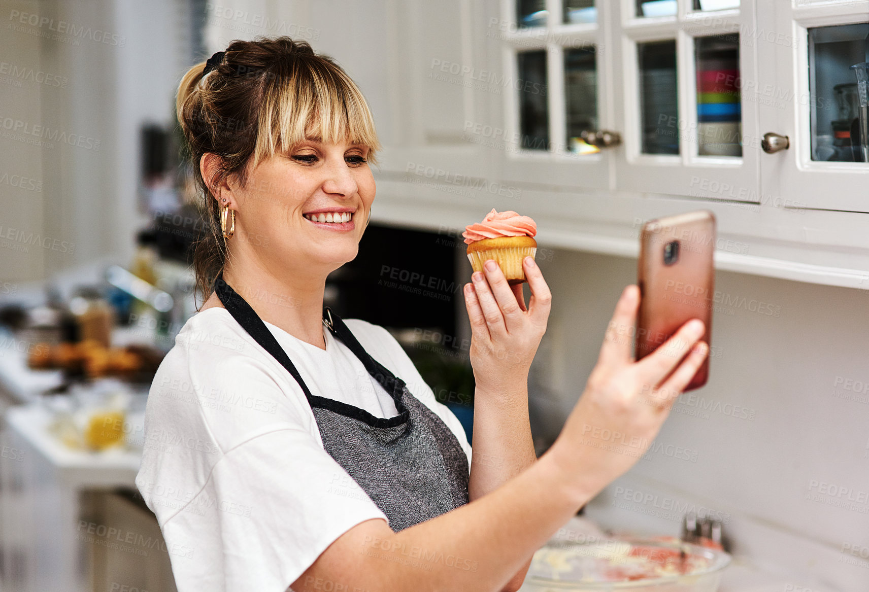 Buy stock photo Baker, happy woman and selfie of dessert in kitchen for social media, show sweets and online blog post in home. Pastry, cupcake and photography of food chef and smile of influencer cooking in house