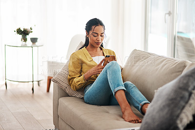 Buy stock photo Cropped shot of an attractive young businesswoman sitting on her couch and using her cellphone while at home
