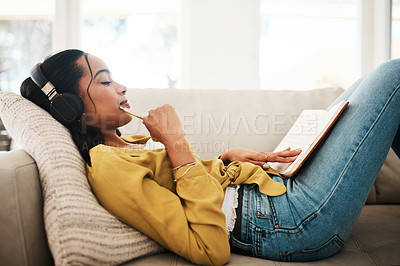Buy stock photo Cropped shot of an attractive young businesswoman lying down on her couch and listening to music while writing notes