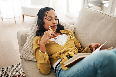 Buy stock photo Cropped shot of an attractive young businesswoman lying down on her couch and listening to music while writing notes