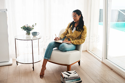 Buy stock photo Full length shot of an attractive young businesswoman sitting alone in her living room and writing notes