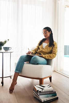 Buy stock photo Full length shot of an attractive young businesswoman sitting alone in her living room and writing notes