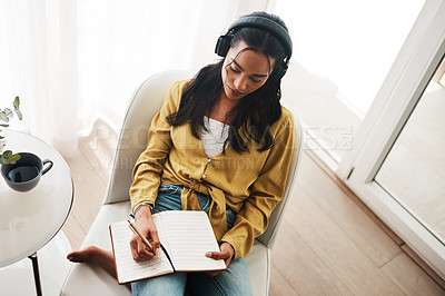 Buy stock photo High angle shot of an attractive young businesswoman sitting in her living room and writing notes while listening to music