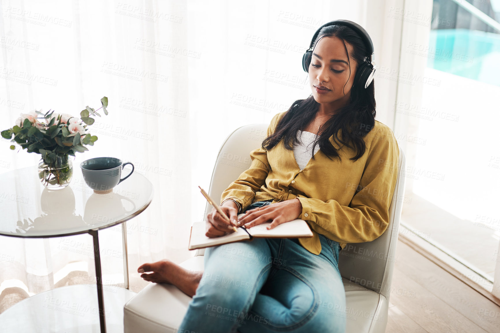 Buy stock photo Cropped shot of an attractive young businesswoman sitting in her living room and writing notes while listening to music