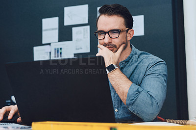 Buy stock photo Cropped shot of a handsome young male architect looking thoughtful while working on a laptop in his office
