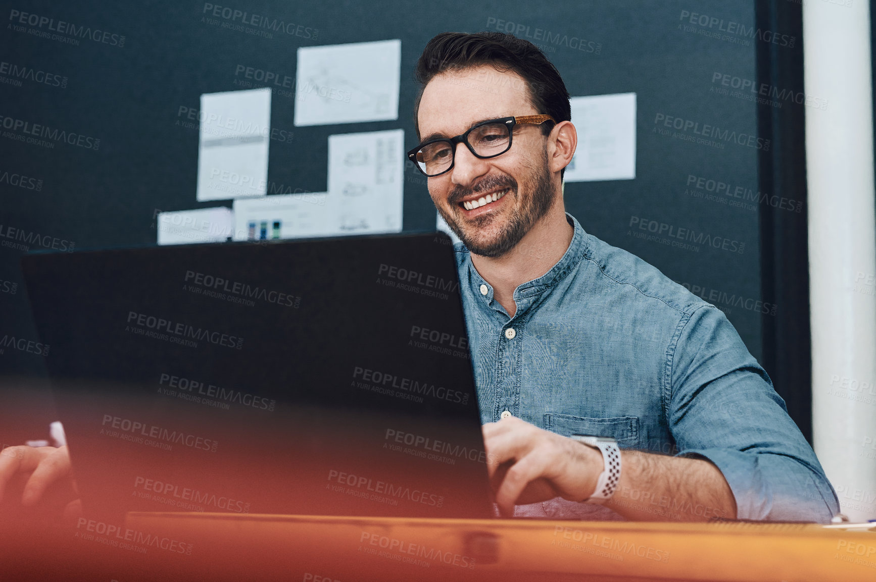 Buy stock photo Cropped shot of a handsome young male architect smiling while working on a laptop in his office