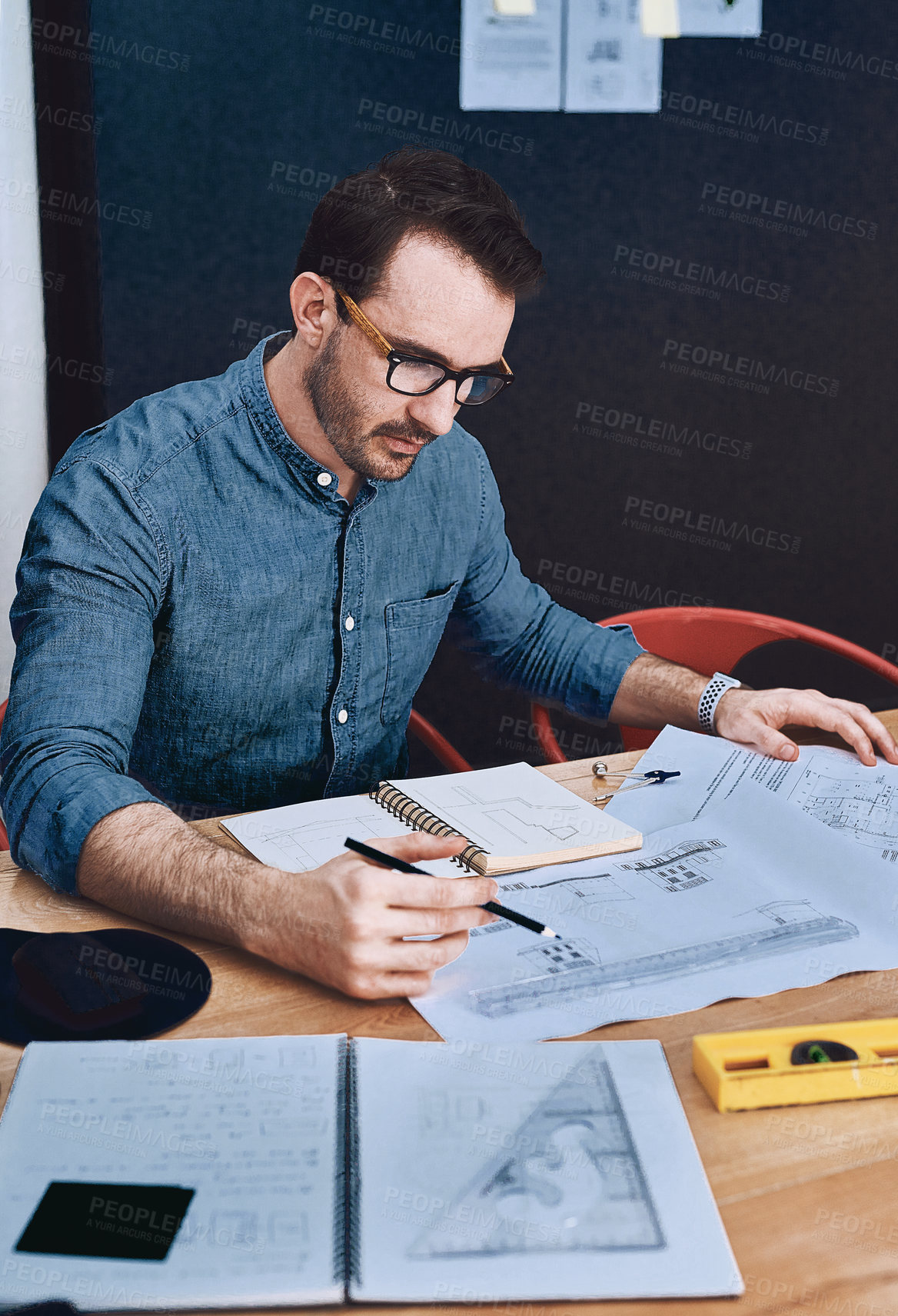 Buy stock photo Cropped shot of a handsome young male architect working with blueprints in a modern office