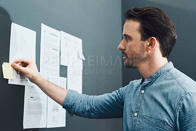 Buy stock photo Cropped shot of a handsome young businessman reading a sticky note while standing in front of a board in a modern office