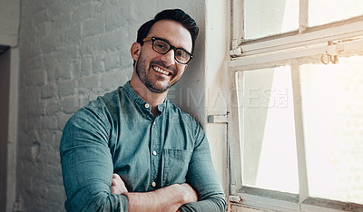 Buy stock photo Cropped portrait of a handsome young businessman smiling while standing with his arms folded in a modern office