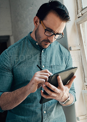 Buy stock photo Cropped shot of a handsome young businessman using a digital tablet while standing in a modern office