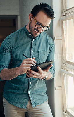 Buy stock photo Cropped shot of a handsome young businessman smiling while using a digital tablet in a modern office