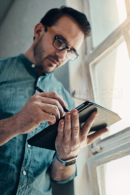 Buy stock photo Cropped shot of a handsome young businessman using a digital tablet while standing in a modern office