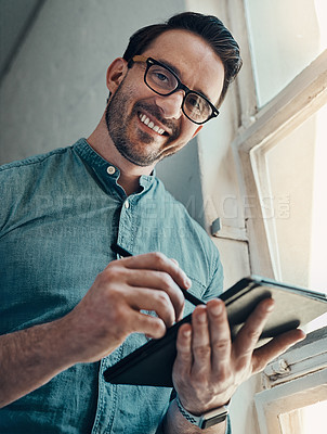 Buy stock photo Cropped portrait of a handsome young businessman smiling while using a digital tablet  in a modern office