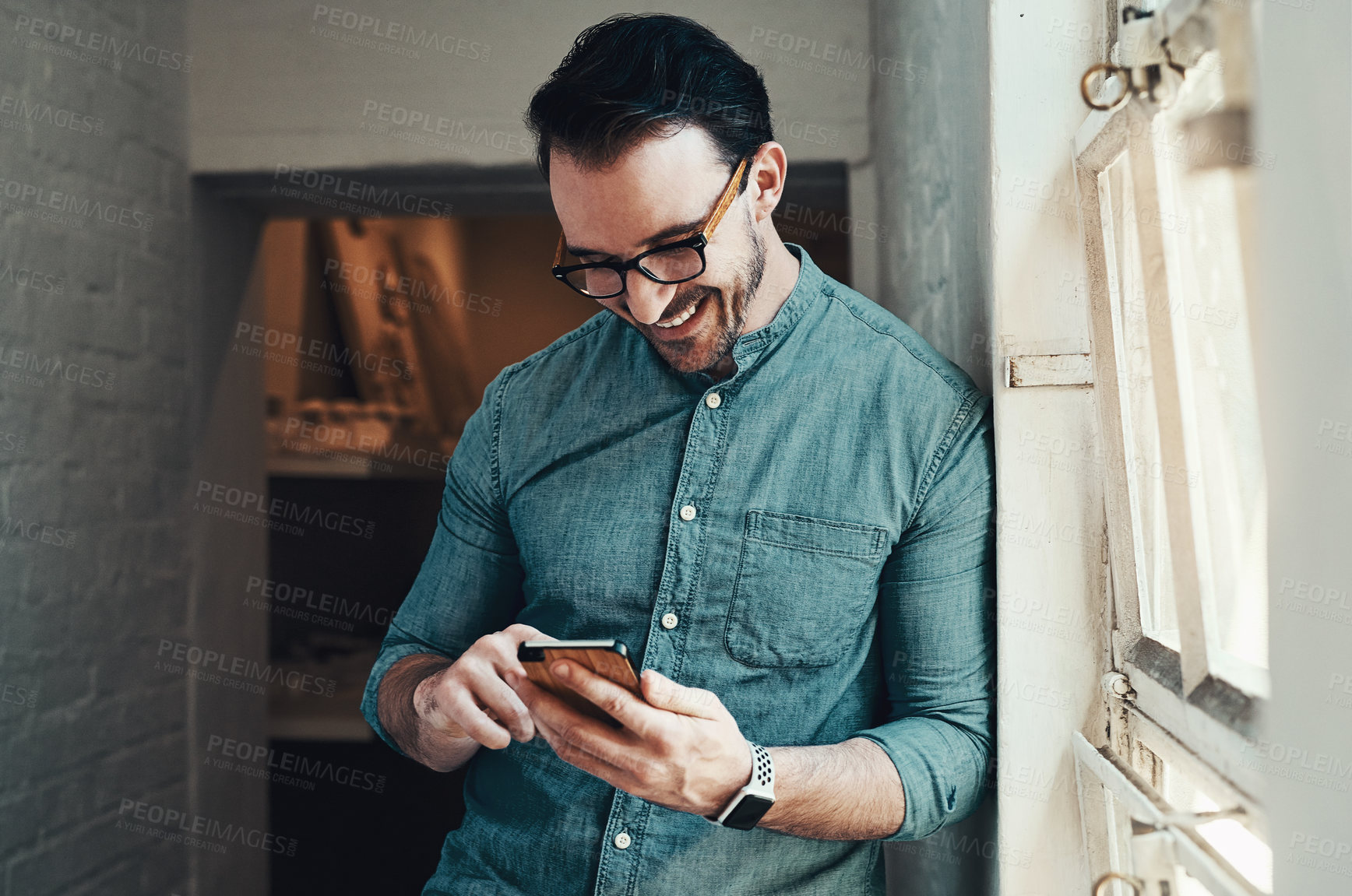 Buy stock photo Cropped shot of a handsome young businessman smiling while using a smartphone in a modern office