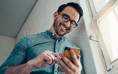 Buy stock photo Cropped shot of a handsome young businessman smiling while using a smartphone in a modern office