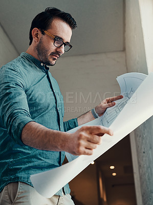 Buy stock photo Cropped shot of a handsome young male architect looking at a blueprint while standing in an office