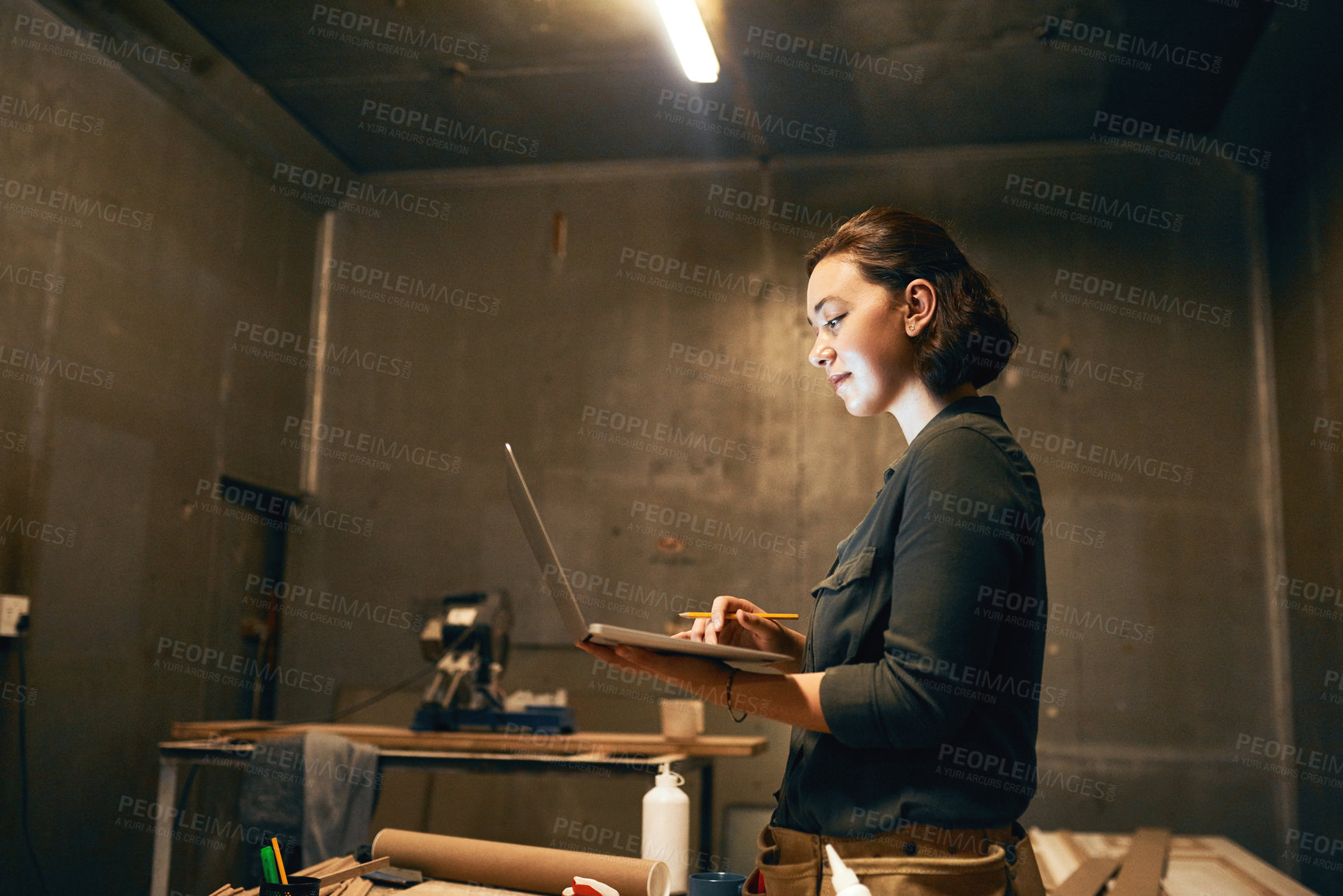 Buy stock photo Cropped shot of an attractive young female carpenter working on her laptop in the workshop