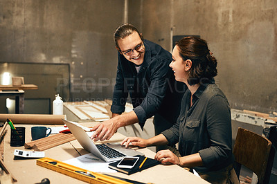 Buy stock photo Cropped shot of two cheerful young carpenters working on a project together while using a laptop inside of a workshop at night