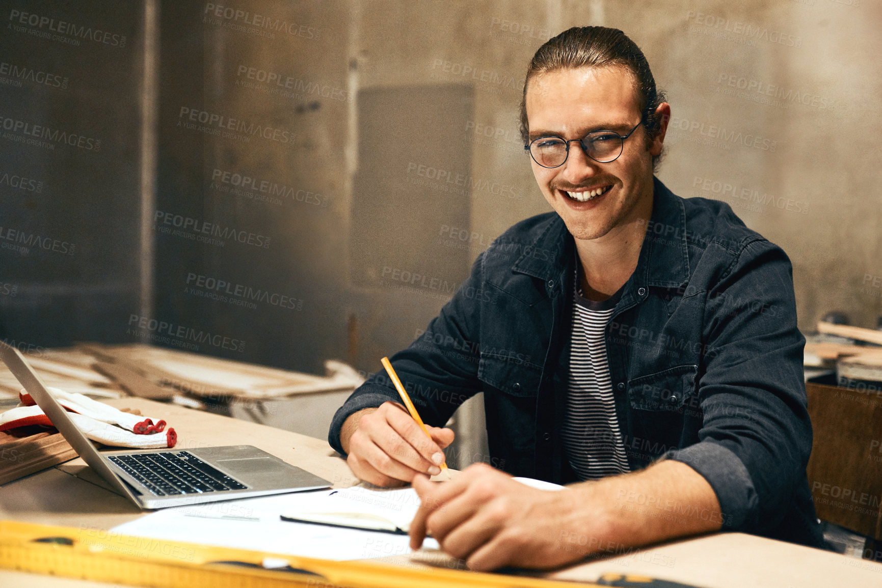 Buy stock photo Portrait of a focused young male carpenter working on a project inside of a workshop at night