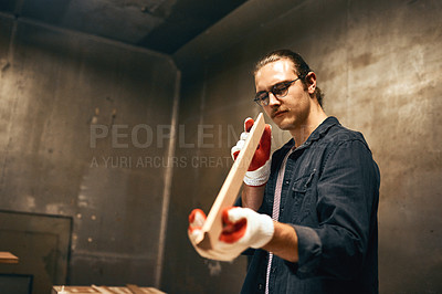 Buy stock photo Cropped shot of a focused young male carpenter holding and examining a piece of wood while working inside of a workshop at night