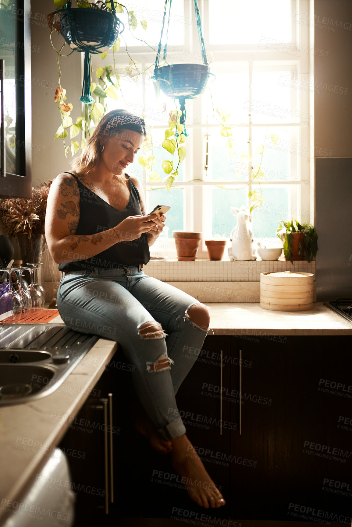 Buy stock photo Shot of a young woman using a smartphone in the kitchen at home