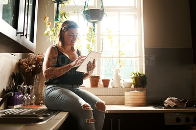 Buy stock photo Trendy woman browsing internet on tablet using her new wifi at home looking happy and satisfied. Normal, real and edgy young female searching online for cool recipe ideas to use in her modern kitchen