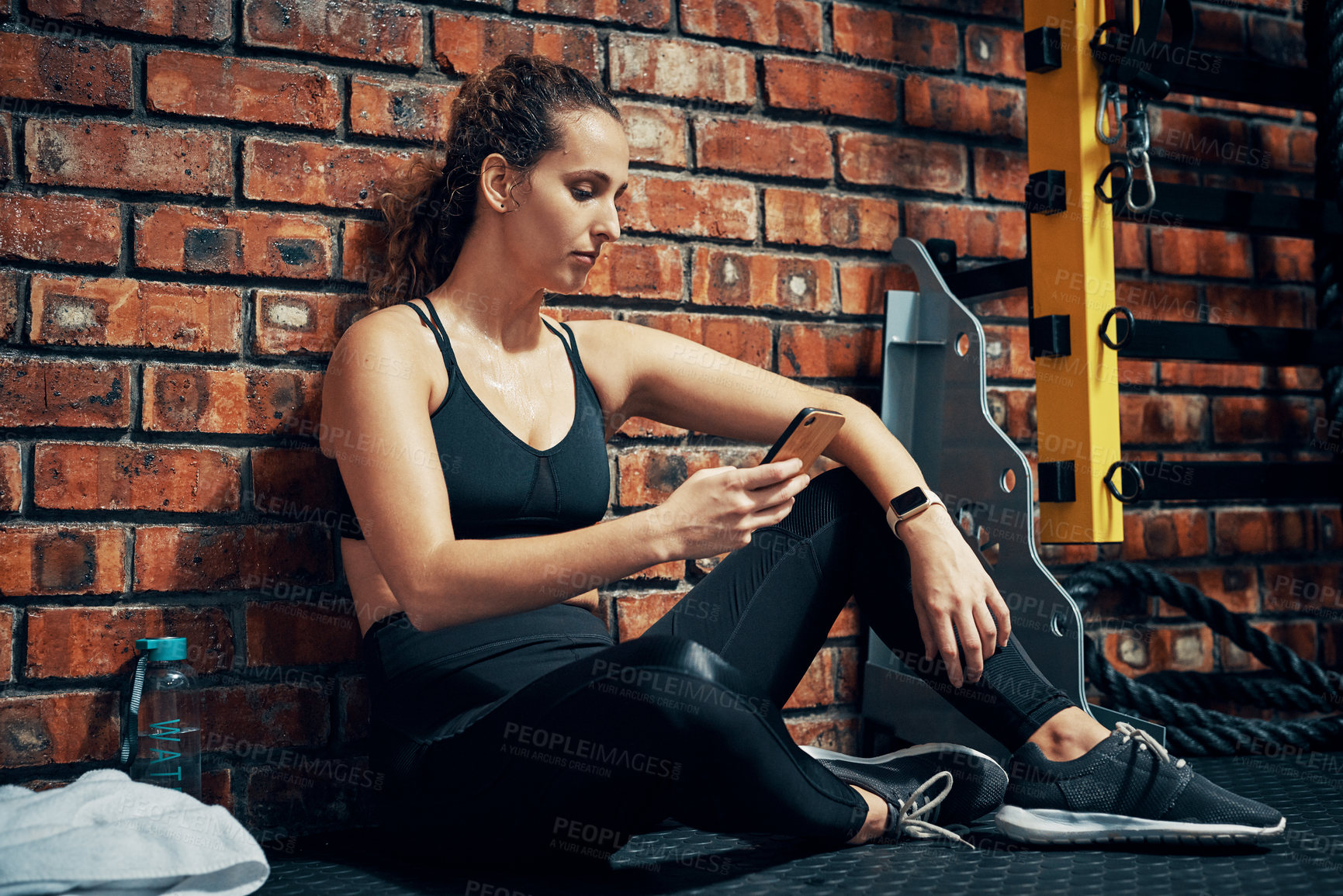 Buy stock photo Shot of a sporty young woman using her cellphone during her break at the gym