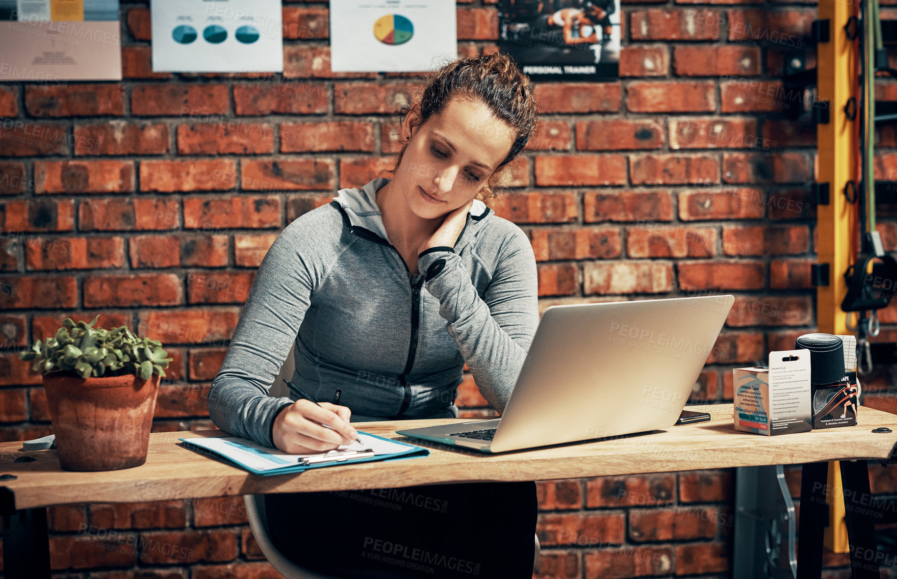 Buy stock photo Cropped shot of a fitness instructor making notes while using a laptop