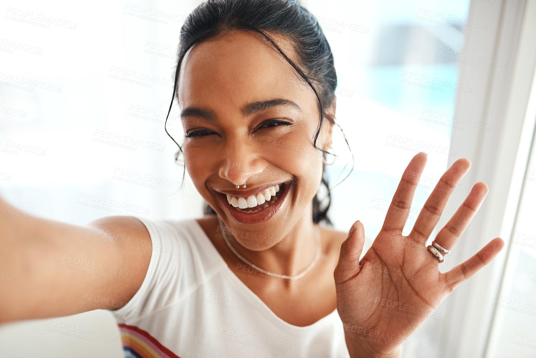 Buy stock photo Cropped portrait of an attractive young blogger standing in her home and waving at the camera during a selfie