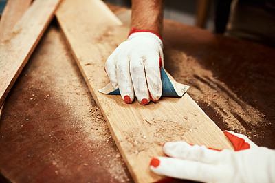 Buy stock photo Closeup of an unrecognizable male carpenter using sandpaper to smoothen out a piece of wood inside of a workshop at night