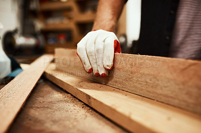 Buy stock photo Closeup of an unrecognizable male carpenter using sandpaper to smoothen out a piece of wood inside of a workshop at night