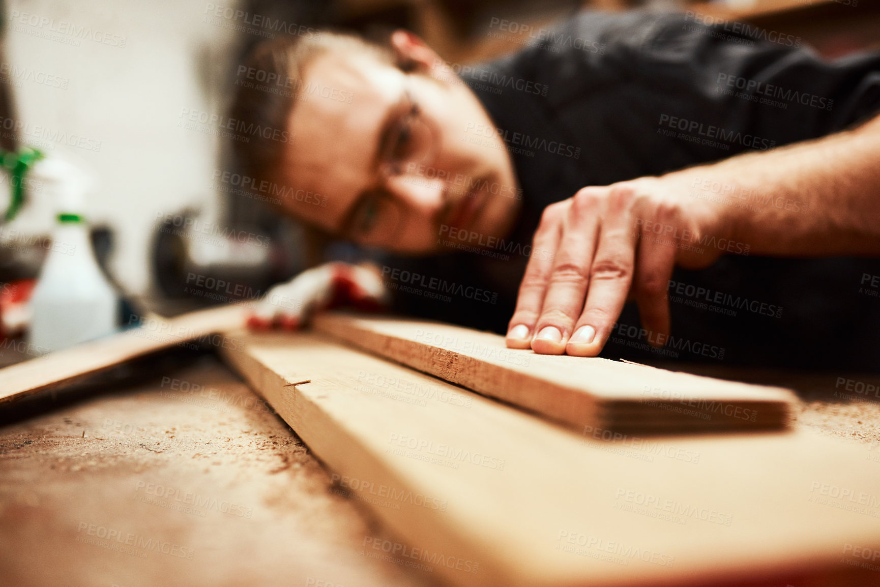 Buy stock photo Cropped shot of a focused young male carpenter blowing dust off of a piece of wood after sanding it inside of his workshop during the night