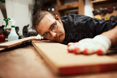 Buy stock photo Cropped shot of a focused young male carpenter blowing dust off of a piece of wood after sanding it inside of his workshop during the night