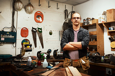 Buy stock photo Portrait of a confident young male carpenter standing with his arms folded inside of his workshop at night
