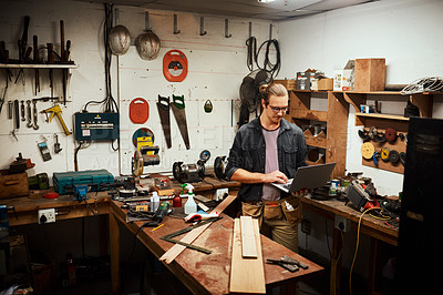Buy stock photo Cropped shot of a focused young male carpenter working on his laptop while standing inside of his workshop at night