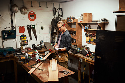 Buy stock photo Cropped shot of a focused young male carpenter working on his laptop while standing inside of his workshop at night