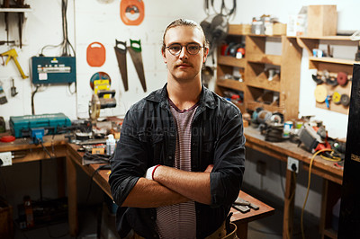 Buy stock photo Portrait of a confident young male carpenter standing with his arms folded inside of his workshop at night