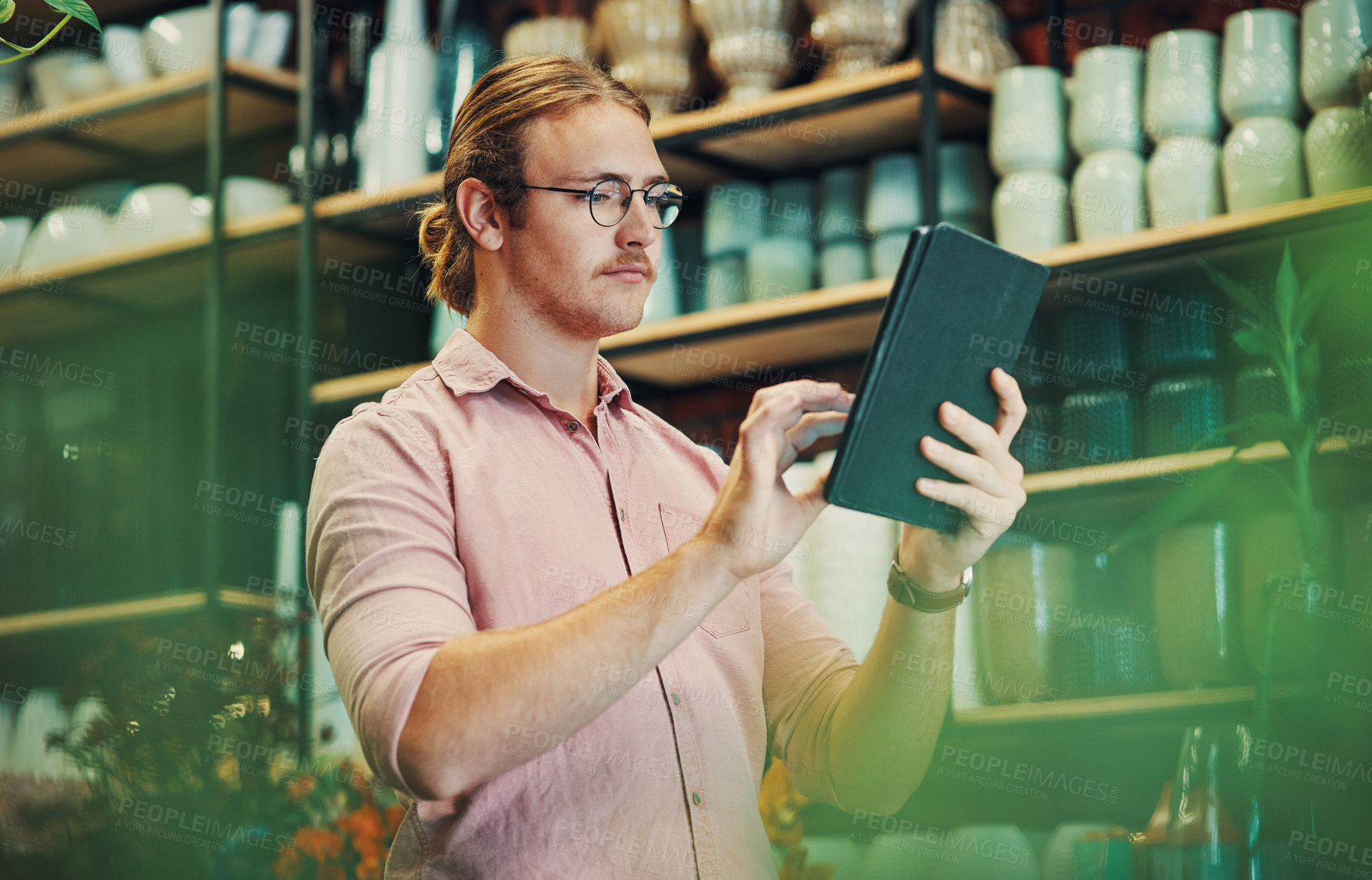 Buy stock photo Cropped shot of a handsome young businessman standing alone in his flower shop and using a tablet
