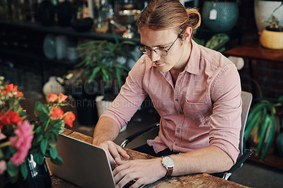 Buy stock photo Cropped shot of a handsome young businessman sitting alone in his floristry and using his laptop