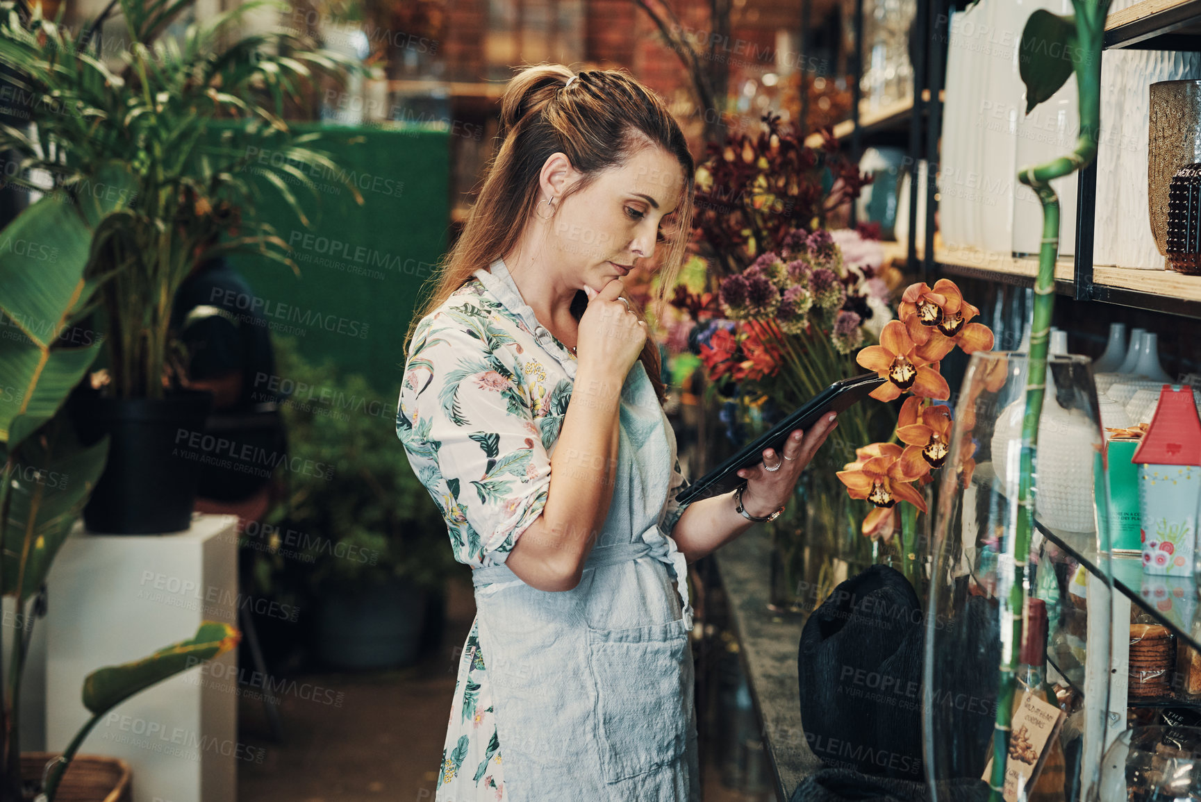 Buy stock photo Cropped shot of an attractive young businesswoman standing alone in her floristry and looking contemplative while using a tablet