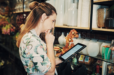 Buy stock photo Cropped shot of an attractive young businesswoman standing alone in her floristry and looking contemplative while using a tablet