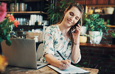 Buy stock photo Cropped shot of an attractive young businesswoman sitting alone in her floristry and making notes while on a phonecall