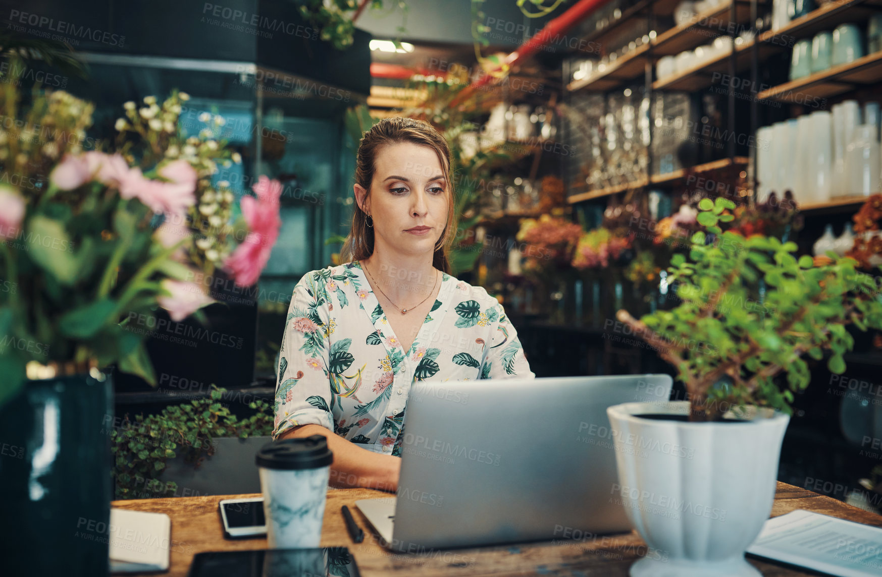 Buy stock photo Cropped shot of an attractive young businesswoman sitting alone in her floristry and using her laptop