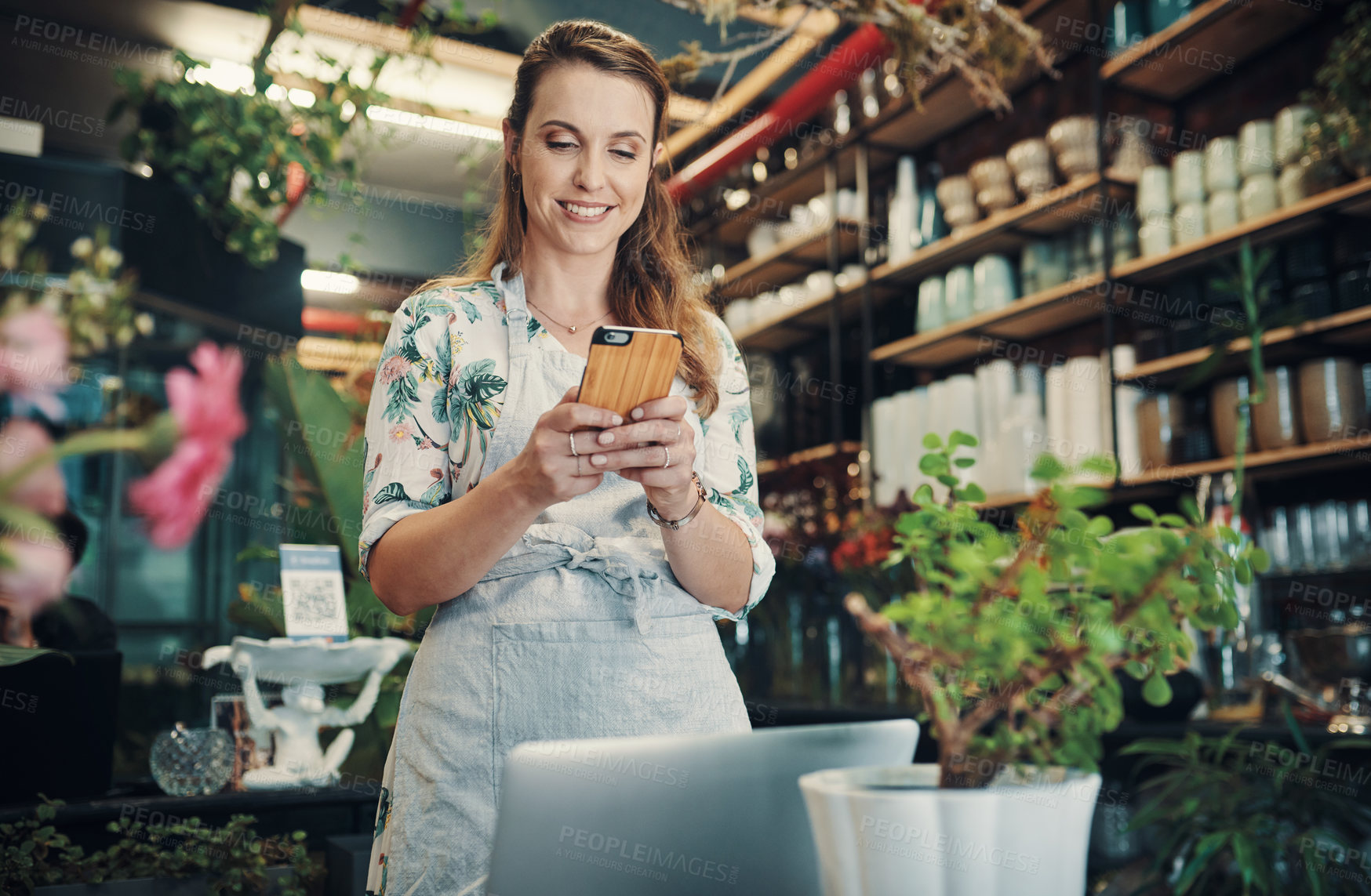 Buy stock photo Cropped shot of an attractive young businesswoman standing in her floristry and using her cellphone to photograph her flowers