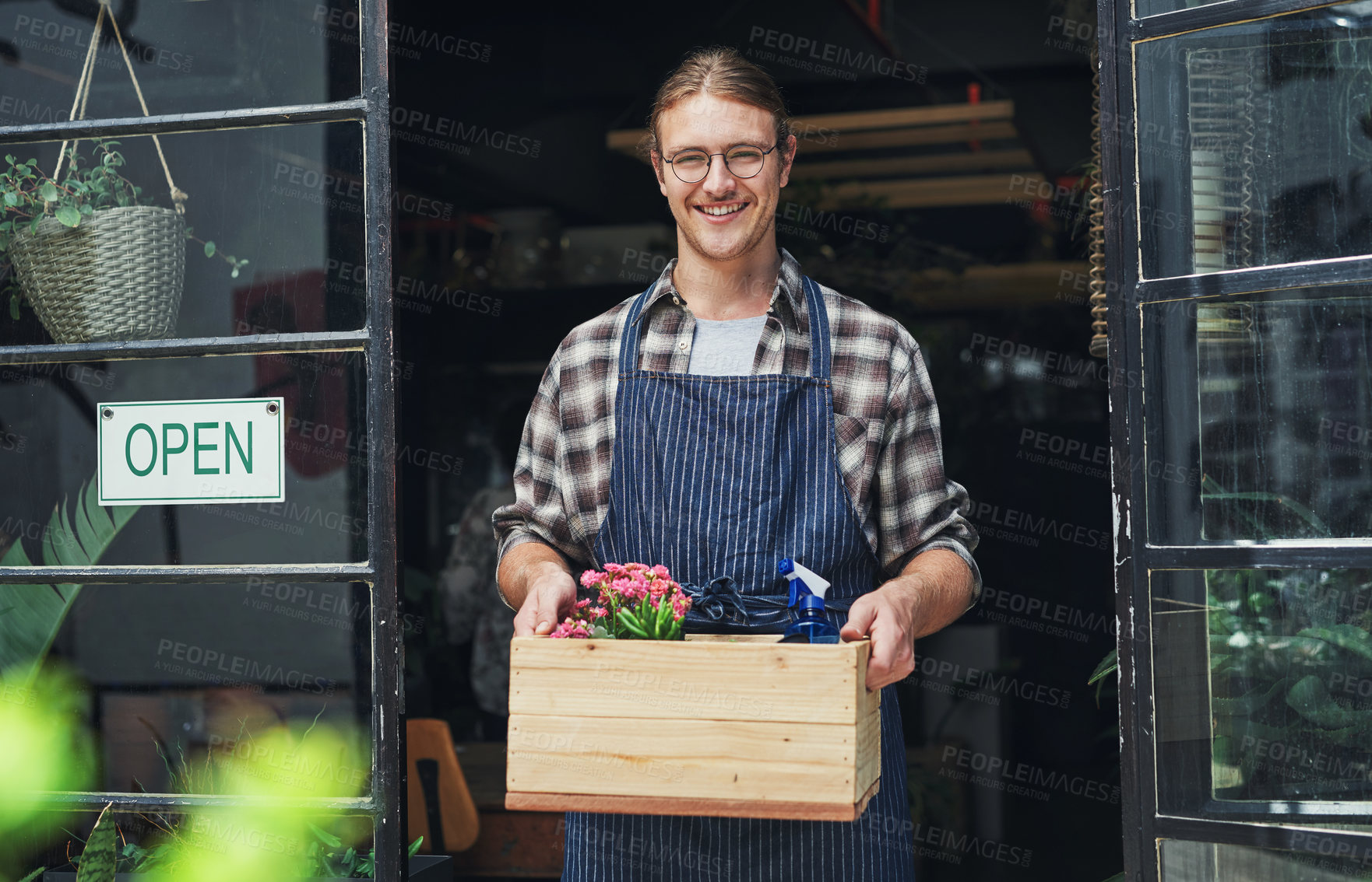 Buy stock photo Cropped portrait of a handsome young business owner holding a crate of flowers at the entrance of his floristry