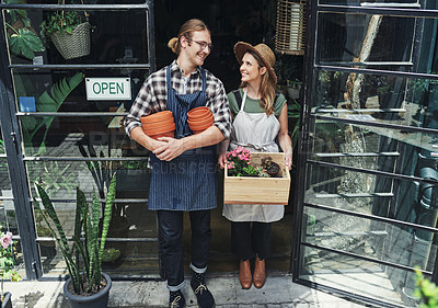 Buy stock photo Full length shot of two young business owners standing at the entrance of their floristry together and holding potting supplies