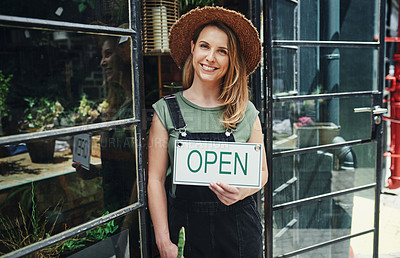 Buy stock photo Cropped portrait of an attractive young business owner standing alone and holding the open sign at the floristry entrance