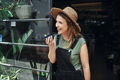 Buy stock photo Cropped shot of an attractive young business owner standing and sending voice notes on her cellphone at the floristry entrance
