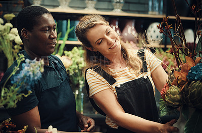 Buy stock photo Cropped shot of two attractive young florists standing together and adjusting the flower arrangements in her shop